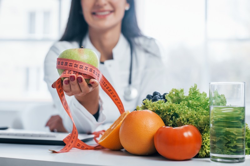 Female nutritionist in white coat sitting indoors in the office at workplace.