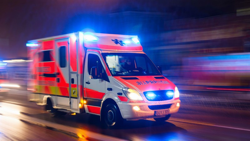 Emergency ambulance speeds through city night with flashing lights and blurred background showing rapid response
