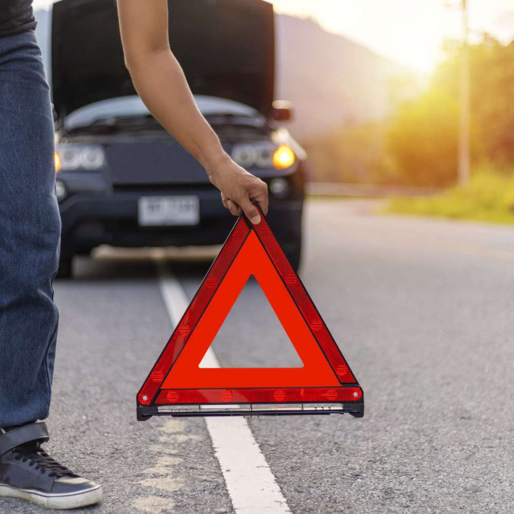 Man hold and put down the red triangle for warning have black color car parking  on road and oper car hood.